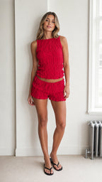 Model wearing the red textured crop top and ruffle shorts set, front view