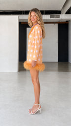 Side profile of model in orange polka dot feather hem dress