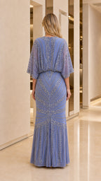 Back view of woman showcasing draped cape sleeves on blue maxi dress