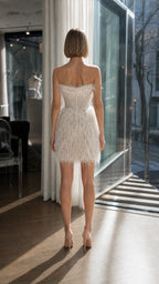 Model wearing white strapless feather mini dress back view