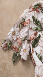 Close-up detail of white mesh fabric with floral embroidery and sequins