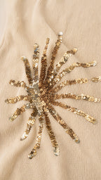 Close-up detail of gold sequin sunburst embroidery on fabric