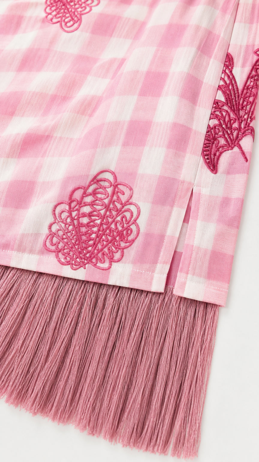 Close-up of pink gingham fabric, embroidery, and fringe hem detail