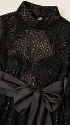 Close-up detail of mock neck, sequin mesh texture, and satin bow