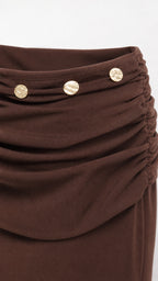 Close-up detail of ruched waistband and metallic buttons on brown mini skirt