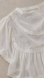 Close-up detail of white top showcasing embroidery and eyelet trim