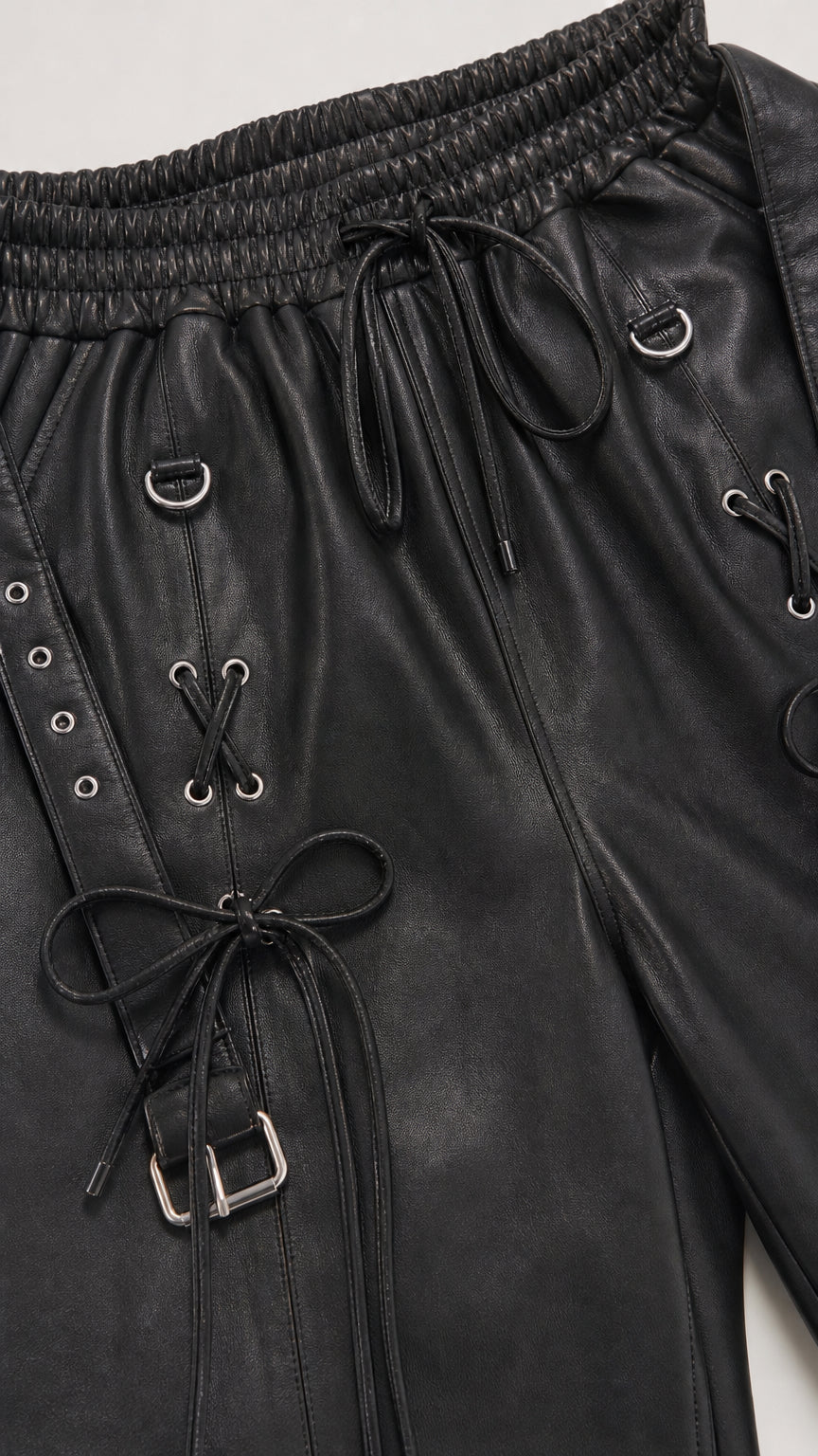 Close-up of black faux leather jogger pants with lace-up details and hardware