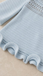 Close-up detail of the open-knit sleeve and ruffled hem in light blue