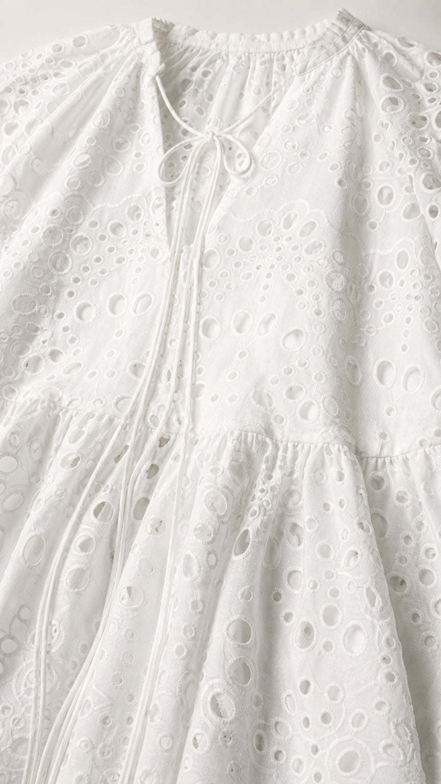 Close-up detail of white eyelet embroidery and tie neckline