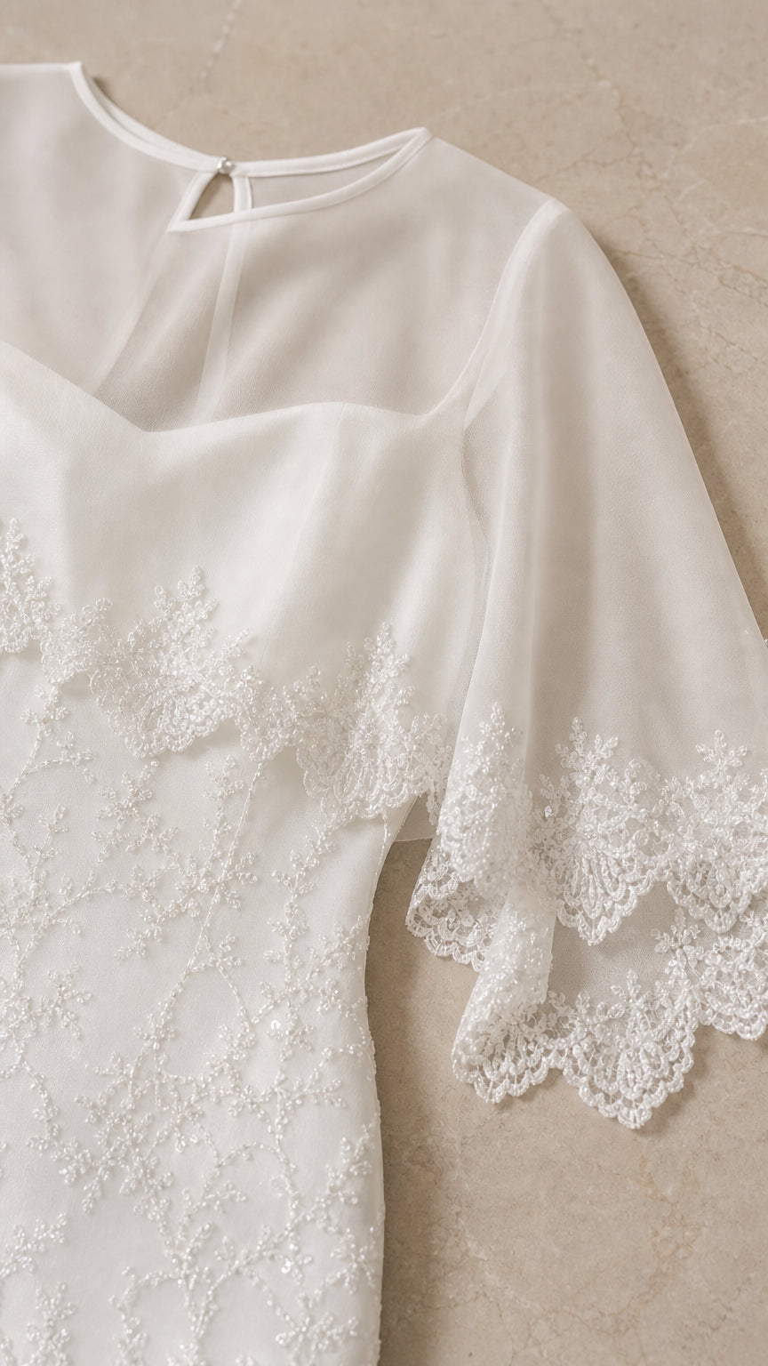 Close-up of sheer cape sleeve and lace trim on white dress