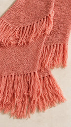 Close-up detail of textured knit fabric and fringe hem in coral