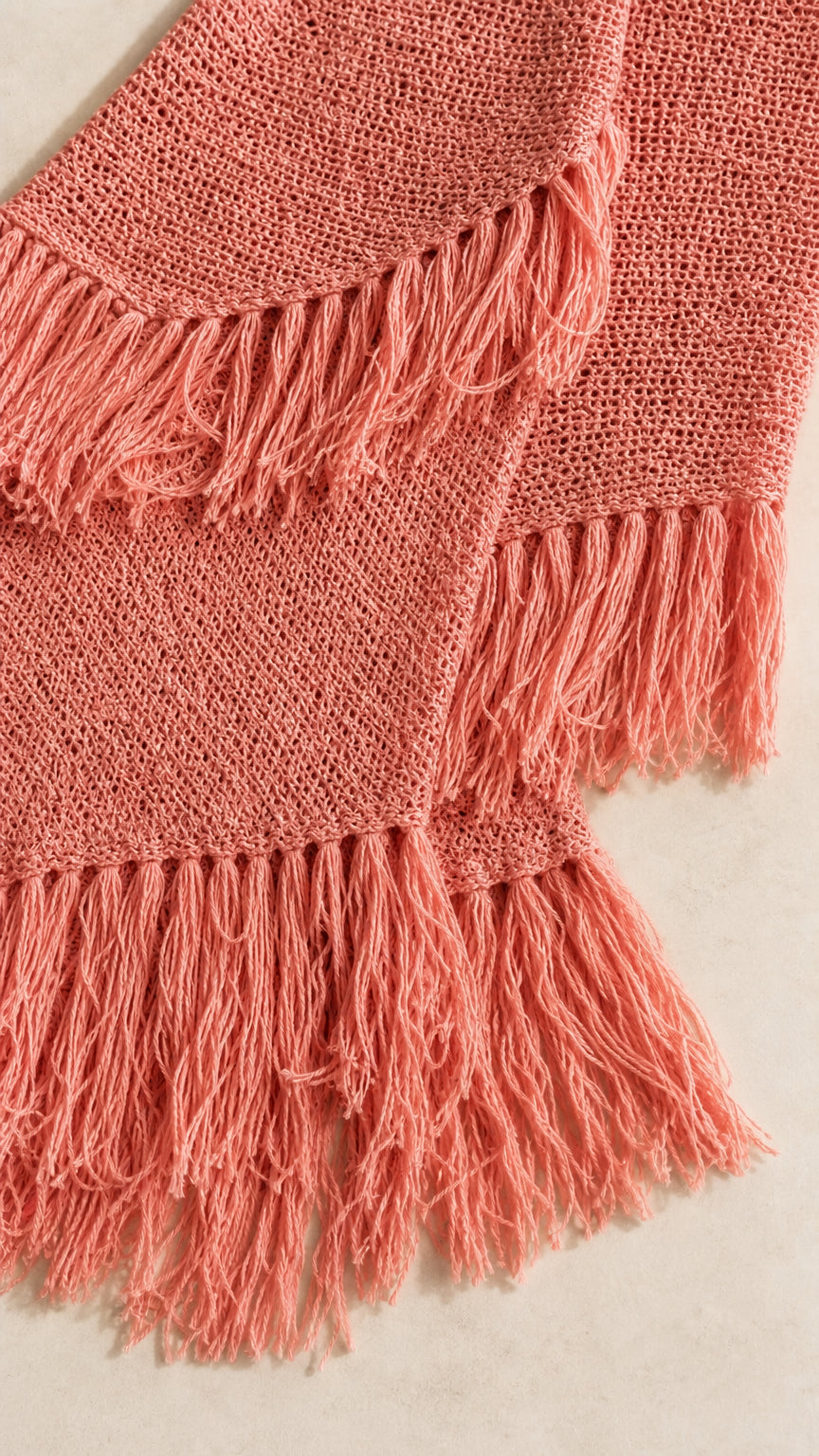 Close-up detail of textured knit fabric and fringe hem in coral