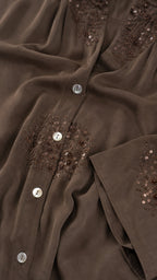 Close-up detail of embroidery and buttons on brown shirt