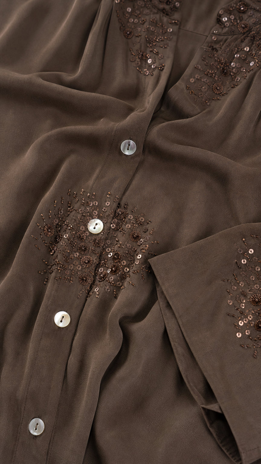 Close-up detail of embroidery and buttons on brown shirt